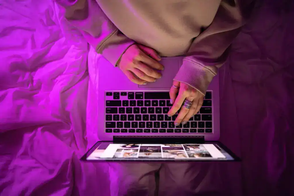 Person using a laptop and tablet for digital workspace management at night.