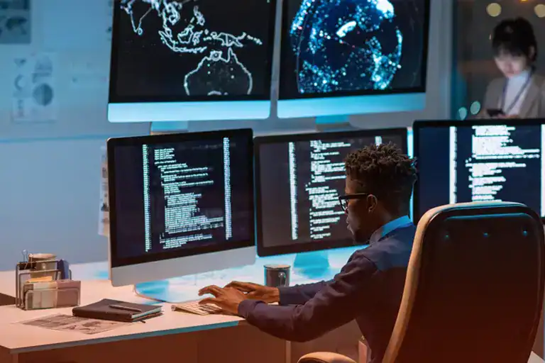 Professional cybersecurity analyst working with multiple monitors displaying data and maps.